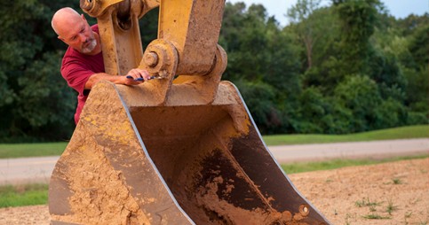 Worker releasing quick hitch on excavator